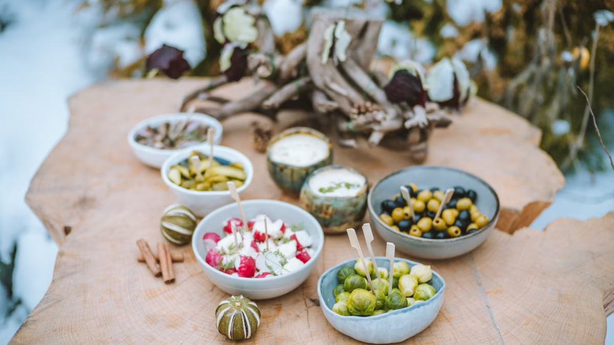A rustic winter spread of appetizers on a wooden surface, featuring vegetables and dips.