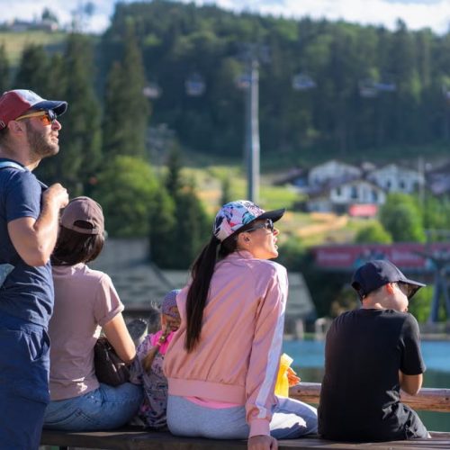 A family enjoys a sunny day sitting on a bench in Bukovel, Ukraine, with scenic mountain views.
