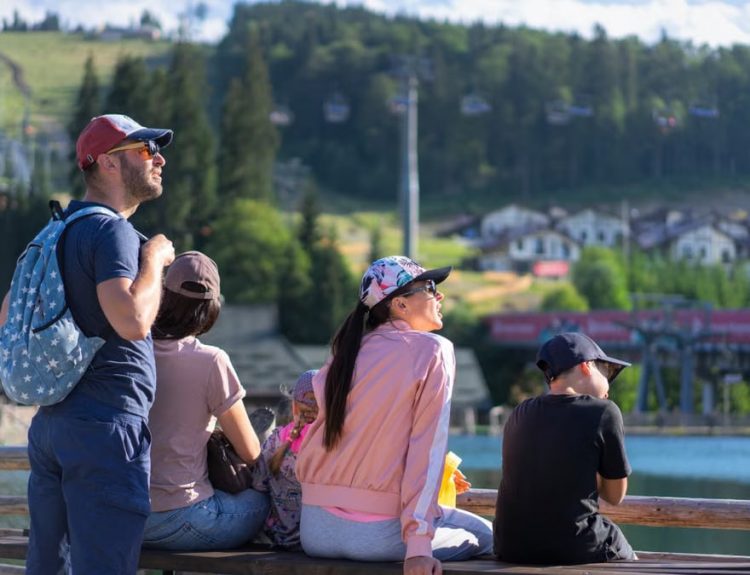 A family enjoys a sunny day sitting on a bench in Bukovel, Ukraine, with scenic mountain views.