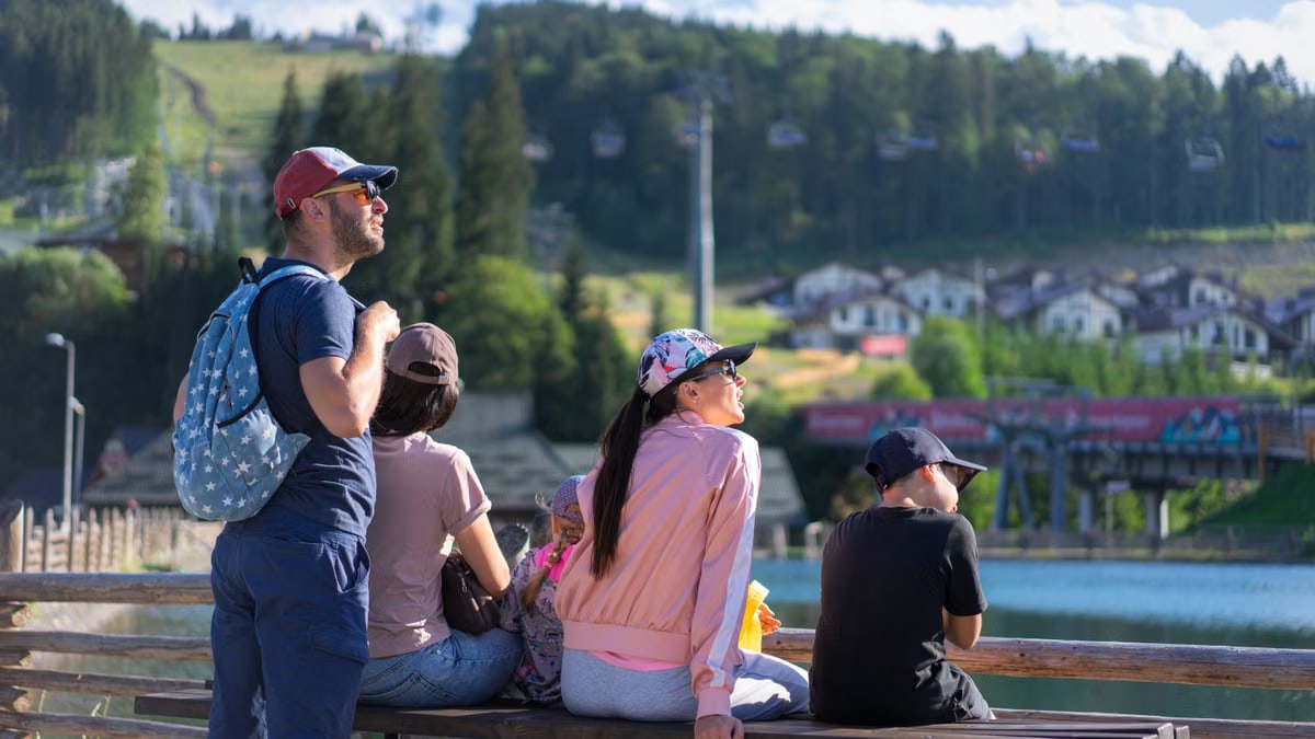 A family enjoys a sunny day sitting on a bench in Bukovel, Ukraine, with scenic mountain views.
